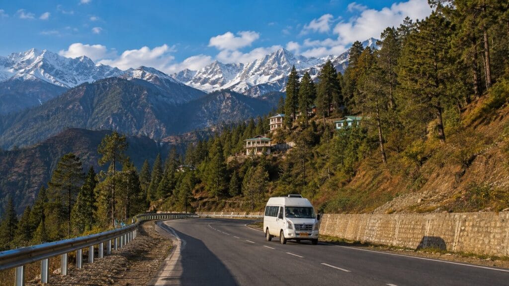 Tempo Traveller on a wide Himachal mountain road with snowy peaks