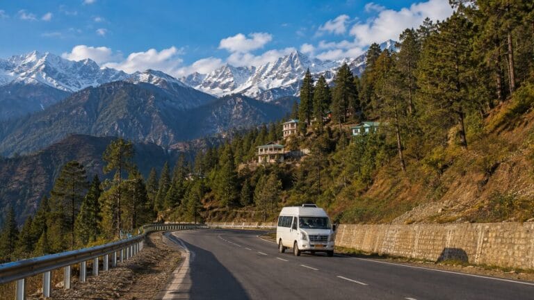 Tempo Traveller on a wide Himachal mountain road with snowy peaks